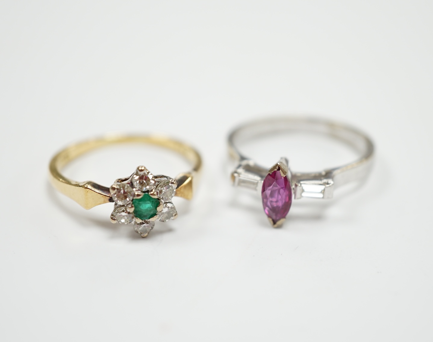 An 18ct, emerald and diamond set flower head cluster ring, size N and an 18ct white metal ruby and diamond set three stone ring, size L/M, gross weight 6.2 grams.